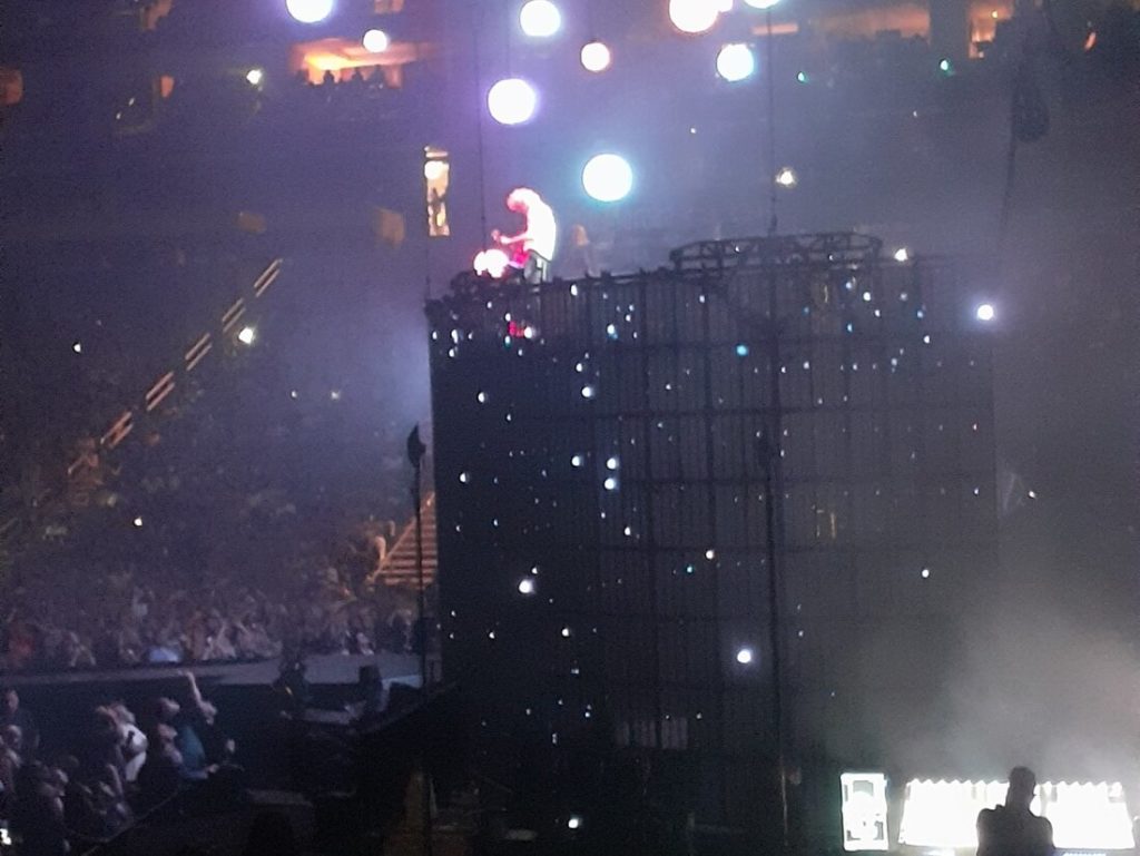 Brian May playing a guitar solo on a raised stage surrounded by planet-shaped lights.