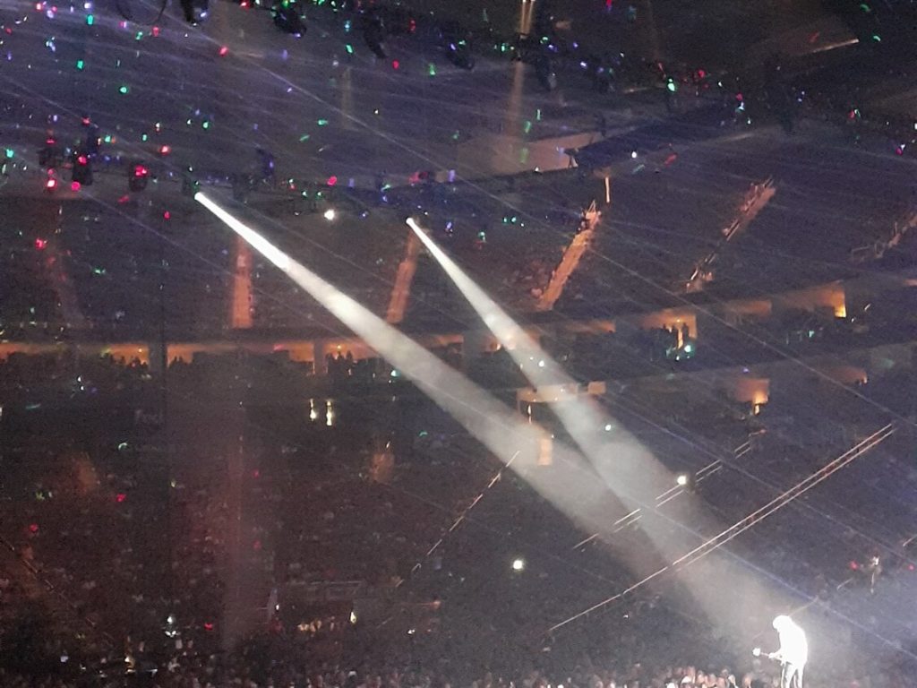 Brian May playing guitar with two spotlights lighting him.