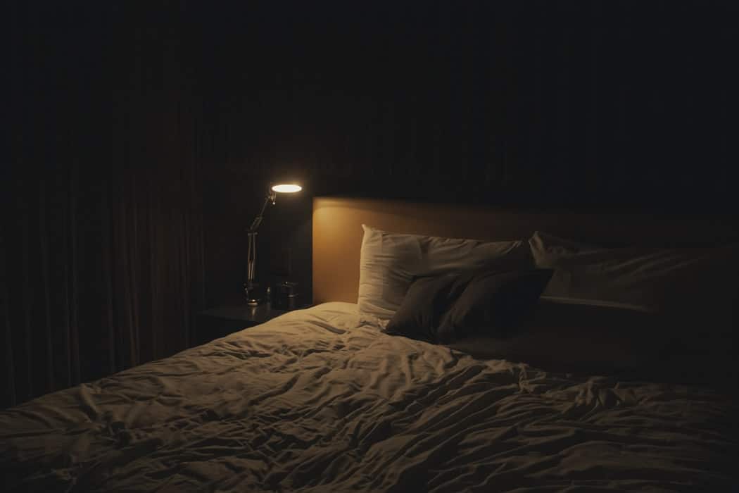 lamp on next to bed in dark room